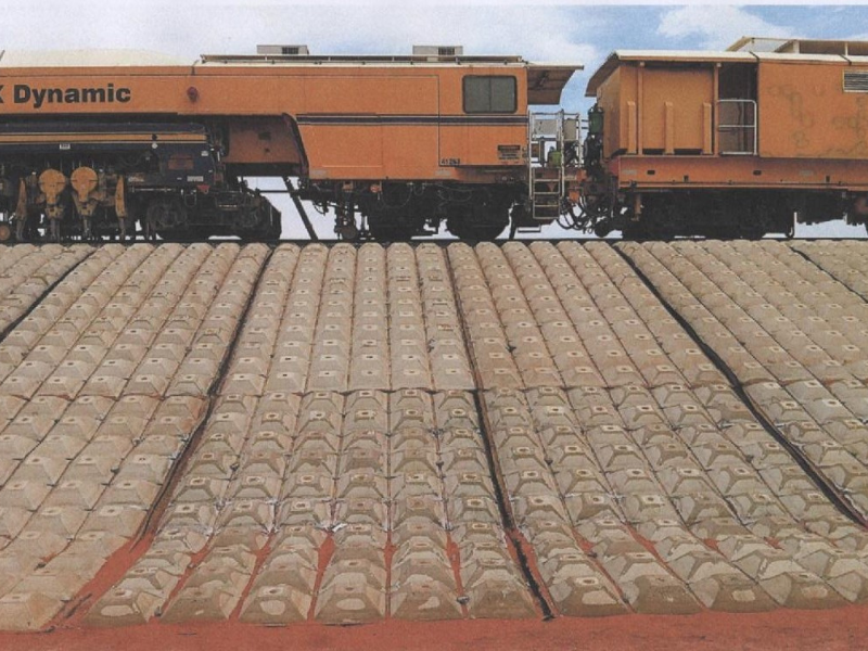 A large orange diesel train engine on tracks, showing Flexmat™ concrete block retainment of rail line